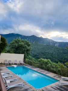 a swimming pool with chairs and mountains in the background at Hôtel Villa Les Orangers in Olmeto