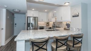 a kitchen with white cabinets and a counter with bar stools at Total Remodel BEACHFRONT 5th Floor - 2 Bd & 2 Ba - Dunes of Panama in Panama City Beach