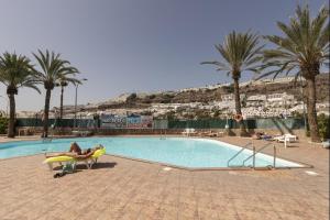 a person sitting in a chair next to a swimming pool at Lightbooking Arizona Puerto Rico in Puerto Rico de Gran Canaria
