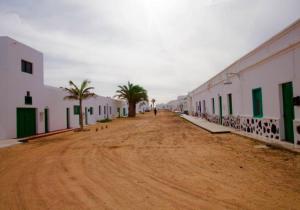 un camino de tierra con palmeras y edificios blancos en Lightbooking La Graciosa, en Caleta de Sebo