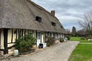 una vieja casa con techo de paja con un camino delante de ella en Chaumière de charme cosy, en Saint-Éloi-de-Fourques