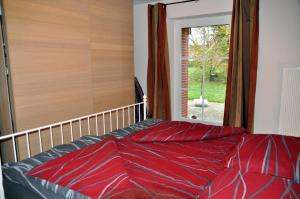 1 cama con sábanas rojas en una habitación con ventana en Petersdorf Ferienwohnung Kleine Auszeit, en Westfehmarn