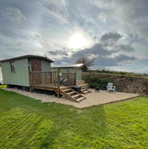 a small green building with a deck and a bench at Oakley View Shepherds Hut with hot tub in Whitby