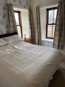 a large white bed in a bedroom with two windows at Cobblers Cottage in St Margaret's Hope