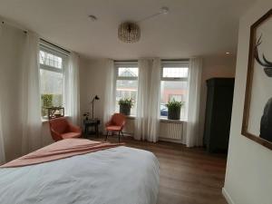 um quarto com uma cama, 2 cadeiras e janelas em B&B het Klontje em Vriescheloo