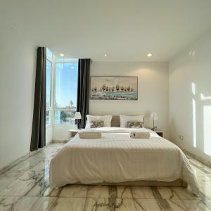a white bedroom with a large bed and a large window at Urban Luxury Apartment in Jeddah