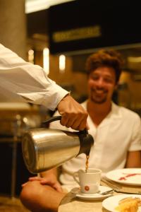 Un hombre está vertiendo café en una taza en Hotel Atlante Plaza, en Recife