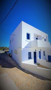 un bâtiment blanc avec des portes bleues sur son côté dans l'établissement Le stanze del tramonto di Eleni, à Lipsi