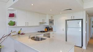 een witte keuken met een wastafel en een koelkast bij Luro 2 - Waterfront Luxury in Ettalong Beach
