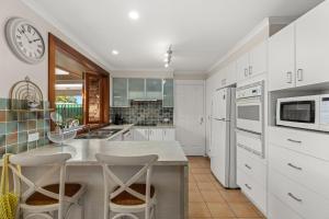 a kitchen with white cabinets and a counter with stools at Crowford Sands by Experience Jervis Bay in Sanctuary Point