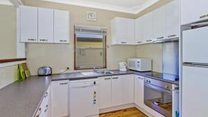 Patonga BeachにあるPatonga Sunset - Waterfront Holiday Houseの白いキャビネットとシンクのあるキッチン