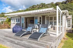 a deck with two chairs and a house at Bach on the Beach - Coast & Country in Onetangi