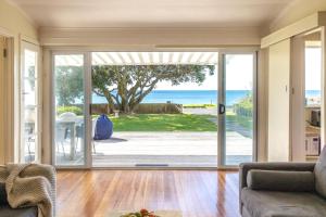 otwarty salon z przesuwnymi drzwiami prowadzącymi do oceanu w obiekcie Bach on the Beach - Coast & Country w mieście Onetangi