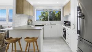 a kitchen with white cabinets and a counter and stools at Sam's Shack Waterfront Woy Woy Bay in Woy Woy