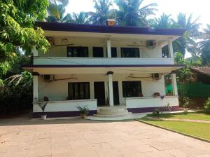 a large white house with palm trees in the background at Heaven Goa Guesthouse in Benaulim