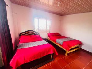 two beds in a room with red sheets and a window at Espectacular casa de campo en finca cafetera in Moniquirá