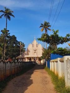 une église derrière une clôture et un chemin de terre dans l'établissement Marari Babu Homestay, à Mararikulam
