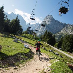 une personne empruntant un vélo sur un chemin de terre à côté d'une remontée mécanique dans l'établissement Hotel Piccola Baita, à Molveno