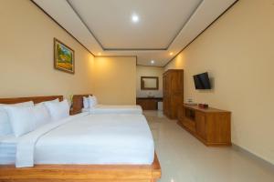 a bedroom with a large white bed and a television at Liliy Guest House Kuta - Badung in Legian