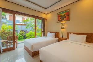 two beds in a hotel room with a window at Liliy Guest House Kuta - Badung in Legian