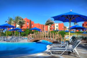 un ponte su una piscina con sedie e ombrelloni blu di Aurora Bay Resort Marsa Alam a Marsa Alam