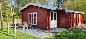 a red shed with a table and chairs in a yard at Vakantiepark 't Urkerbos - 5 persoons Brabantse blokhut in Urk