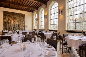 un restaurante con mesas y sillas blancas y ventanas en Priorij Corsendonk en Oud-Turnhout