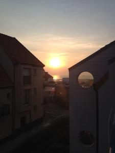 a sunset behind two buildings with the sun in the distance at Loft, terrasse au soleil - Vue mer, à deux pas de tout in Wissant
