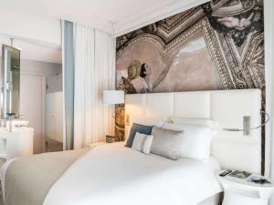 a bedroom with a white bed and a painting on the wall at Cures Marines Hotel & Spa Trouville - MGallery Collection in Trouville-sur-Mer