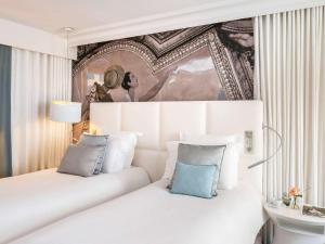 a bedroom with a white bed with blue pillows at Cures Marines Hotel & Spa Trouville - MGallery Collection in Trouville-sur-Mer