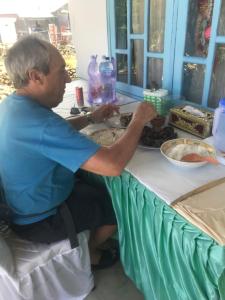 Hogarista Homestay في Kaledupa: رجل كبير في السن يجلس على طاولة مع الطعام