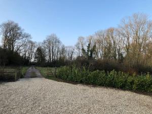 a gravel road with a fence and bushes and trees at The Cowshed in Salisbury