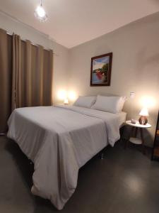 1 dormitorio con 1 cama blanca grande y 2 lámparas en TEMPO FLATS E HOSPEDAGEM, en Alto Paraíso de Goiás