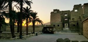 a building with palm trees in front of a sunset at HabuHeritageHomeStayInLuxor in Al Aqālitah