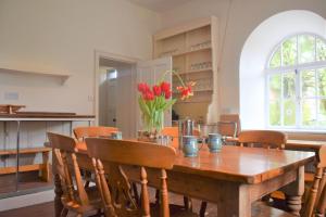 a dining room with a wooden table with red tulips at Coachmans Cottage in Carsethorn