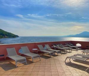 eine Reihe von Stühlen und Tischen auf einer Terrasse neben dem Wasser in der Unterkunft Hotel Pai in Torri del Benaco