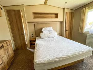 una camera da letto con letto, lenzuola e cuscini bianchi di Beautiful Caravan With Sea Views At California Cliffs In Scratby Ref 50010oc a Great Yarmouth
