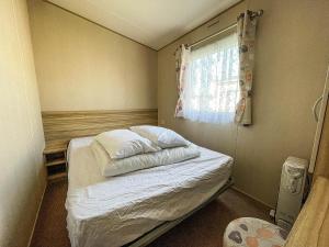 Lovely 8 Berth Caravan At Broadland Sands Near Great Yarmouth Ref 20161bs في Hopton on Sea: سرير صغير في غرفة مع نافذة