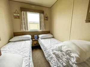 two beds in a small room with a window at Lovely Caravan With Decking And Free Wifi In Lowestoft Ref 12106b in Lowestoft