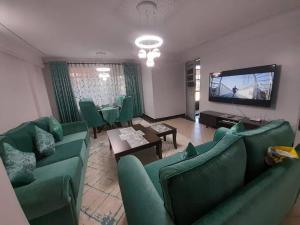 a living room with green couches and a flat screen tv at Gamtoos House:Lovely 3 Bedroom House in Naivasha