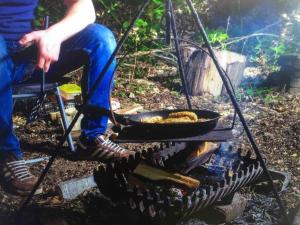 a person sitting next to a grill with a frying pan at Hobbity Bell Hobbity log burner - Hobbity stay in Canterbury
