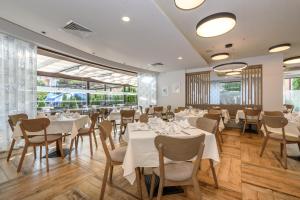 um restaurante com mesas e cadeiras brancas e janelas grandes em Lion Sunny Beach Hotel em Sunny Beach
