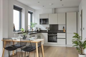 una cocina con armarios blancos y una mesa de madera con sillas. en Kings Oak House by Viridian Apartments, en Londres
