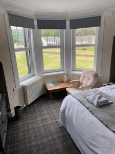 a bedroom with a bed and a chair and two windows at No 4 Portpatrick B&B in Portpatrick