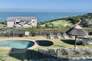 a pool with chairs and an umbrella and a house at Lifestyle Villa at Pinnacle in Mossel Bay