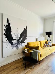 a living room with a yellow couch and black wings painting at Apartamenty Wrzeszcz by Q4Apartments in Gdańsk