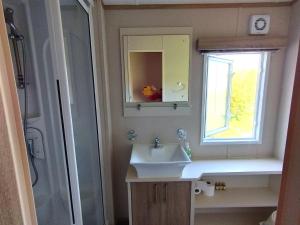 ein Bad mit einem Waschbecken, einem Spiegel und einer Dusche in der Unterkunft Sand Le Mere Holiday Village Caravan hire in Tunstall