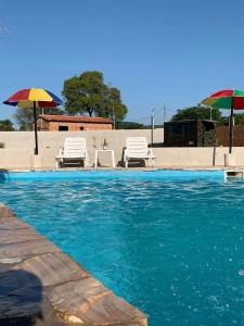 a swimming pool with two chairs and an umbrella at Quinta Coki in Pirayú