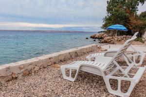 two white chairs and an umbrella on a beach at Apartmani Bošnjak in Starigrad