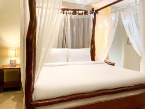 um quarto com uma cama de dossel com lençóis e almofadas brancos em Serene La Playa Boracay em Boracay